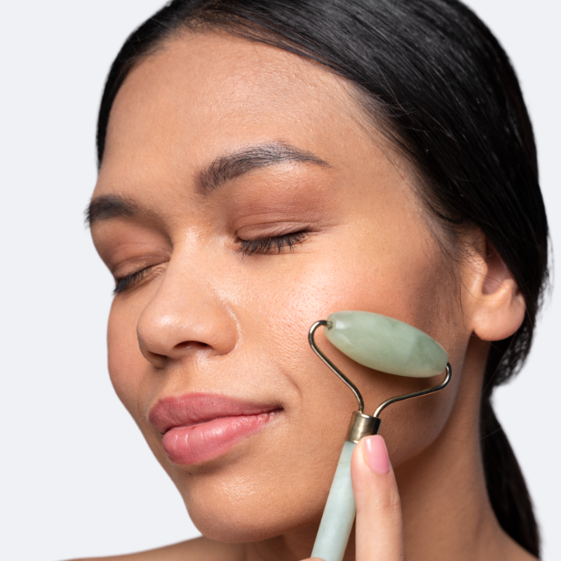 Femme utilisant le rouleau de massage visage en jade vert VELURA sur sa joue