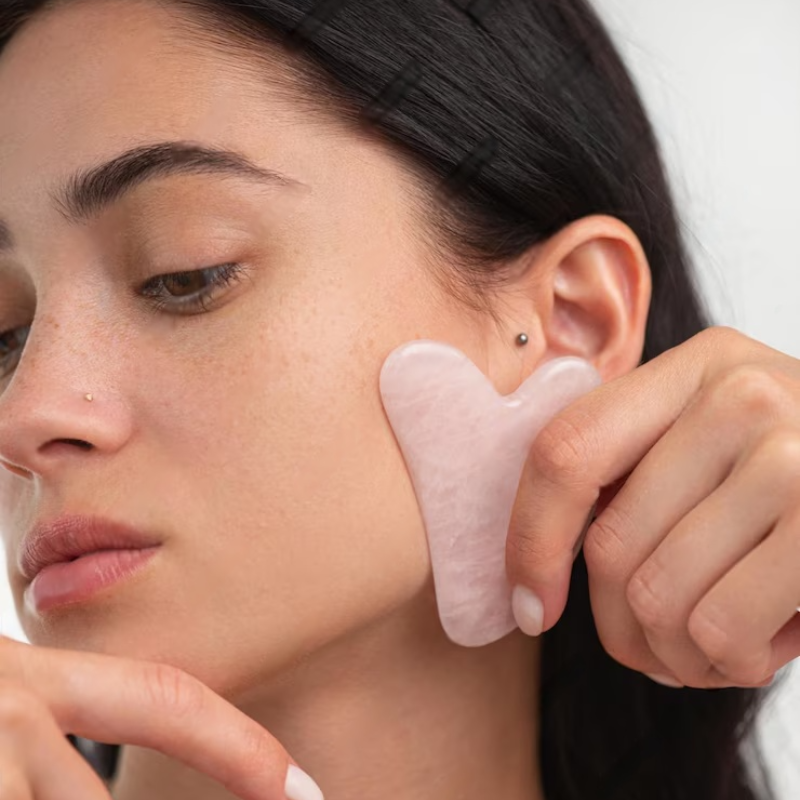 Femme massant sa joue avec la pierre de gua sha en quartz rose VELURA